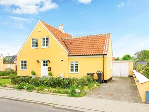 Ein gelbes, zweistöckiges Haus mit einem Ziegeldach, einer Haustür und einem kleinen Garten.