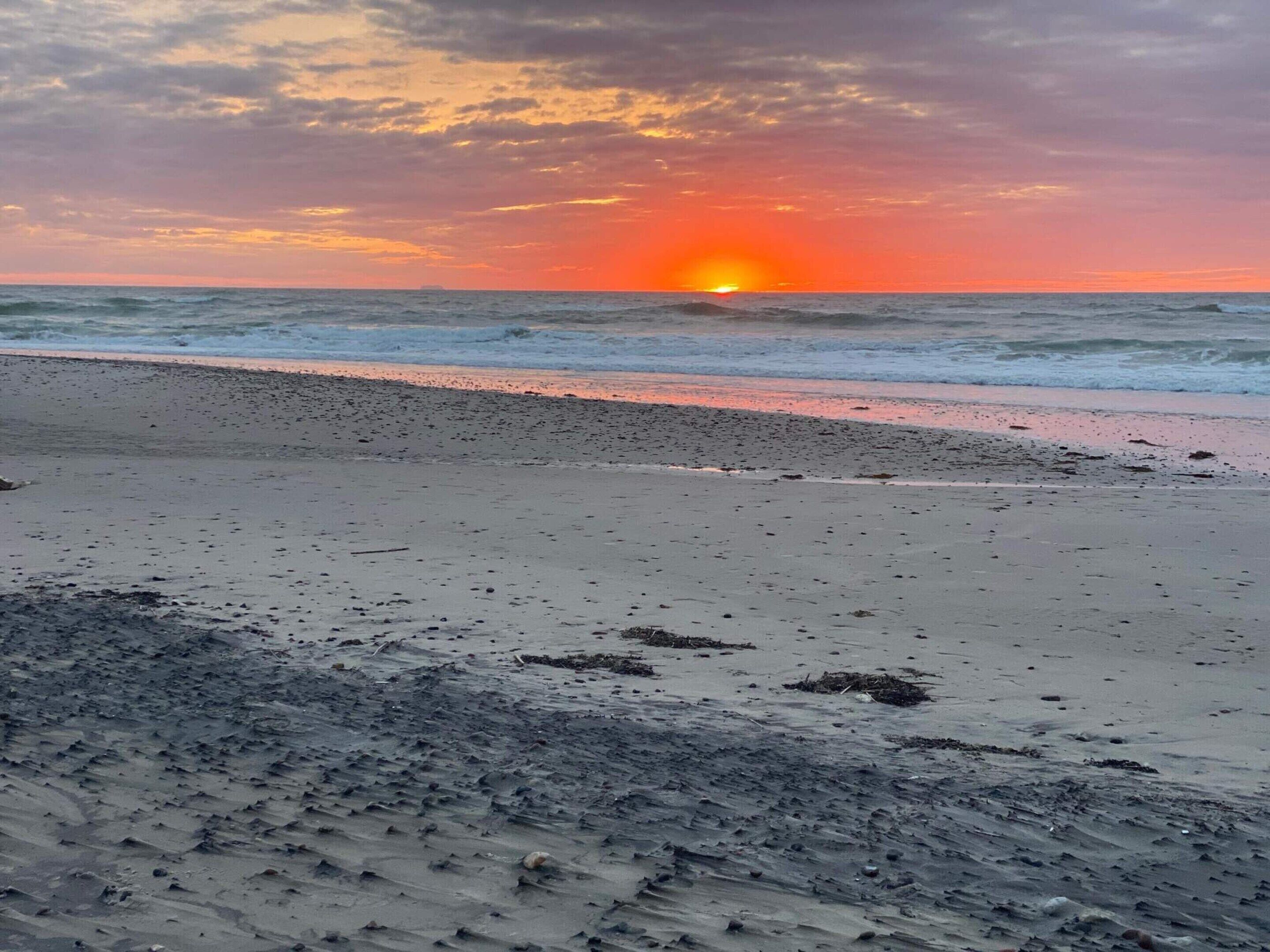 Ein Strand mit Sonnenuntergang, Wellen und wolkenlosem Himmel.