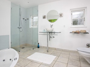 A bathroom with a glass shower enclosure, a white bathtub, a glass sink with a white basin, and a round mirror.