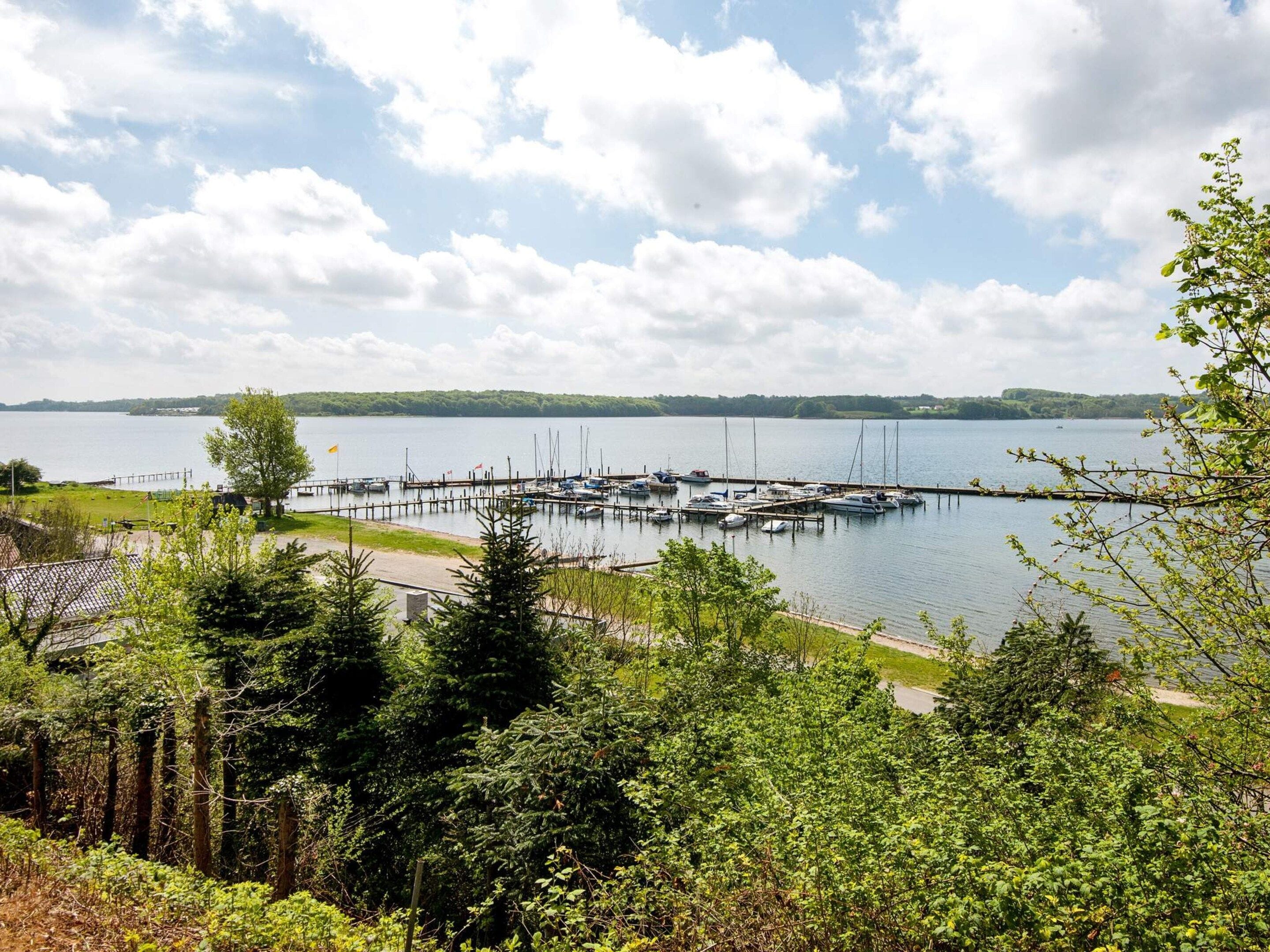 A marina with boats docked, surrounded by dense greenery and a clear sky.