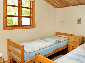 A single wooden bed with a blue mattress in a room with white walls and a wooden ceiling.