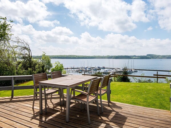 A wooden deck with a table and chairs overlooking a marina with boats.