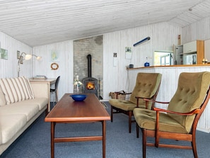 A cozy living room with a fireplace, a sofa, two armchairs, a wooden coffee table, and a blue bowl.