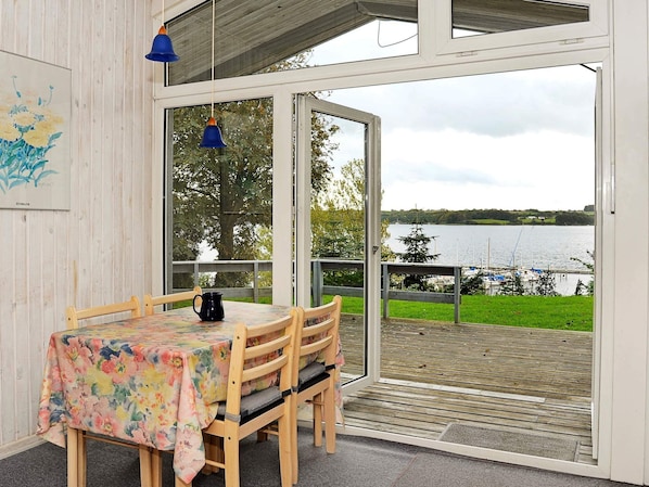 A dining area with a table and chairs, a view of a lake, and a wooden deck.