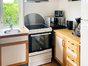 A compact kitchen with a sink, a stove, a microwave, and wooden cabinets. - 4 Person Holiday Home in Broager (Broager)