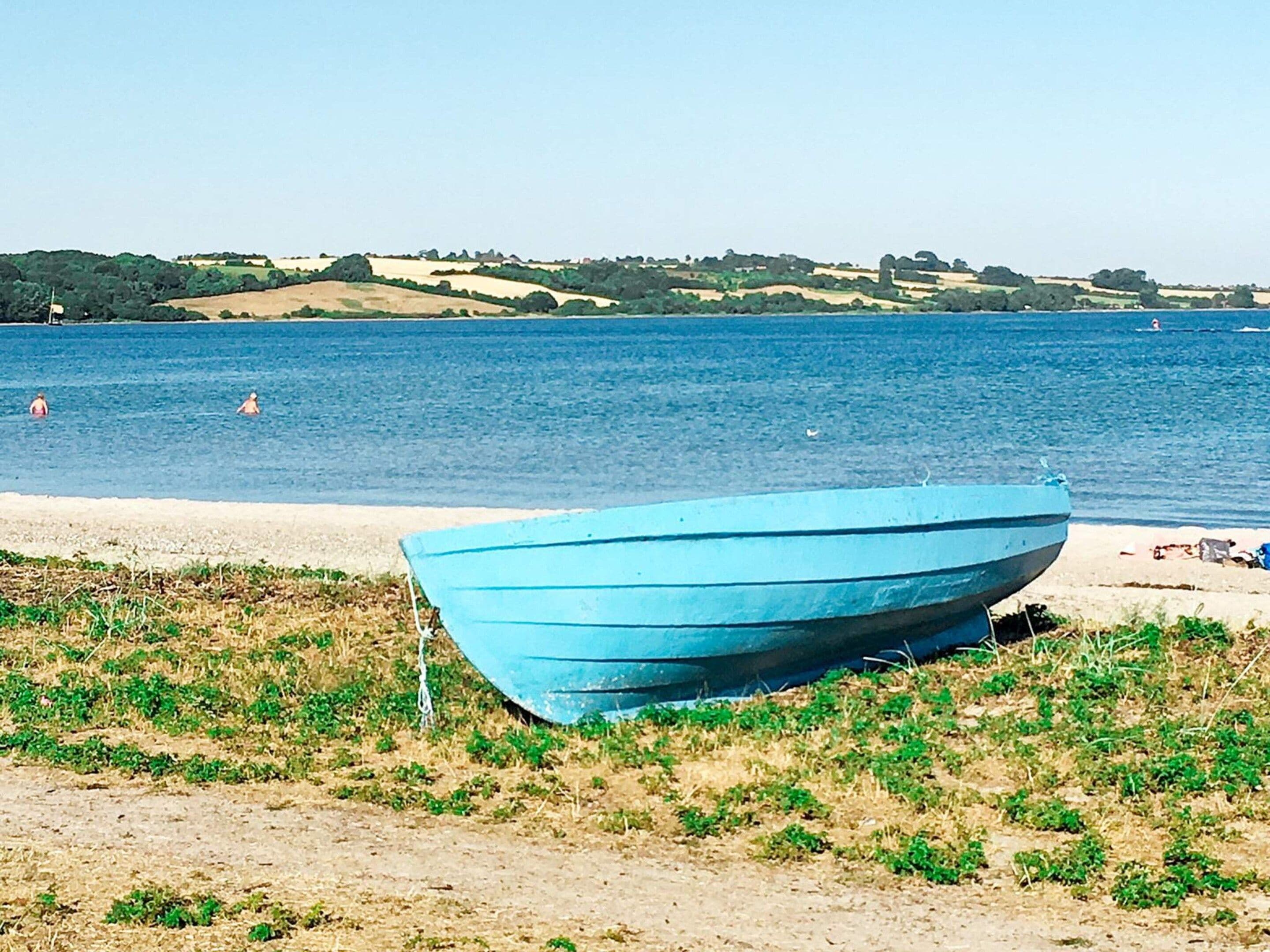 A boat on a sandy beach with water in the background and hills in the distance.