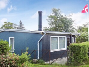A single-story building with a chimney, a flag, and a fenced area with vegetation. - 4 Person Holiday Home in Broager (Broager)