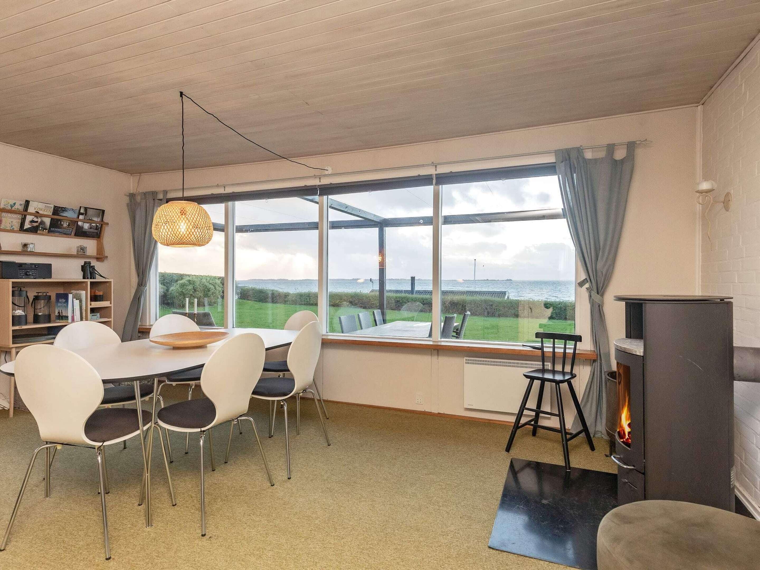 A dining area with a table and chairs, a bookshelf, a large window with a view, and a fireplace.