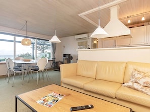 A living room with a sofa, a coffee table with a magazine, a dining area with chairs, and pendant lights.