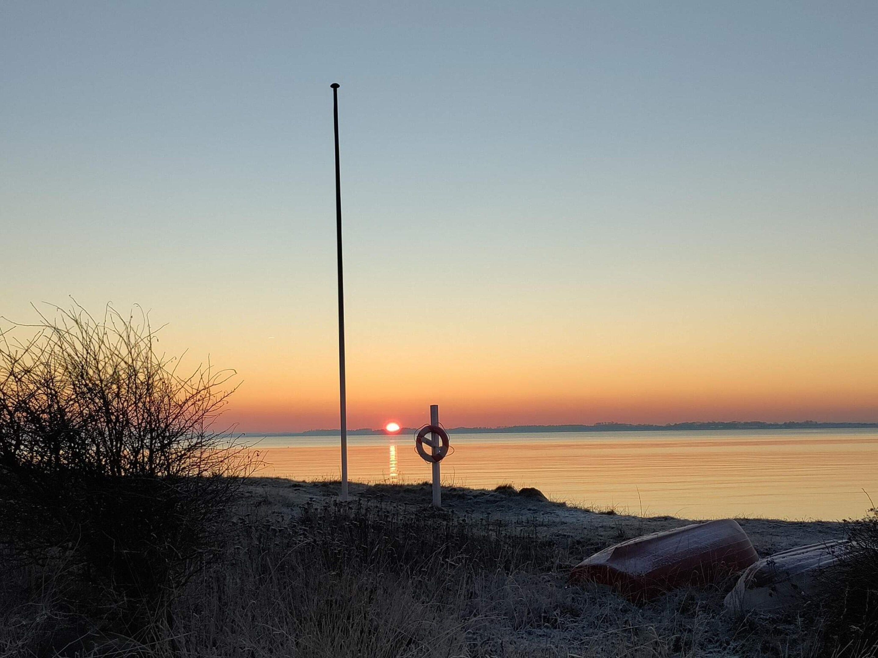 A sunset view with a calm body of water, a lifebuoy, and a boat on the shore.