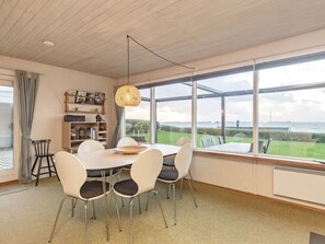 A dining area with a round table and chairs, a hanging light fixture, and a view of the sea through large windows. - 6 Person Holiday Home in Assens (Assens)
