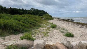 Ein Strand mit einem felsigen Vordergrund, einer grasbewachsenen Hügelkuppe und dem Meer im Hintergrund.
