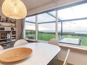 A room with a large window, a table, a chair, a bookshelf, and a hanging light fixture.