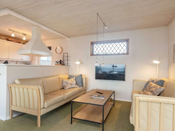 A living room with a sofa, a coffee table, a TV, and a kitchen area in the background.