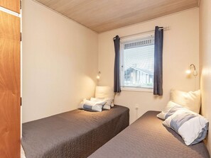 A small room with two beds, a window with curtains, and a wall-mounted light fixture.
