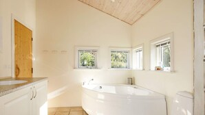 A bathroom with a freestanding bathtub, a toilet, and a sink. There are three windows providing natural light. - 5 Star Holiday Home in Vestervig (Vestervig)