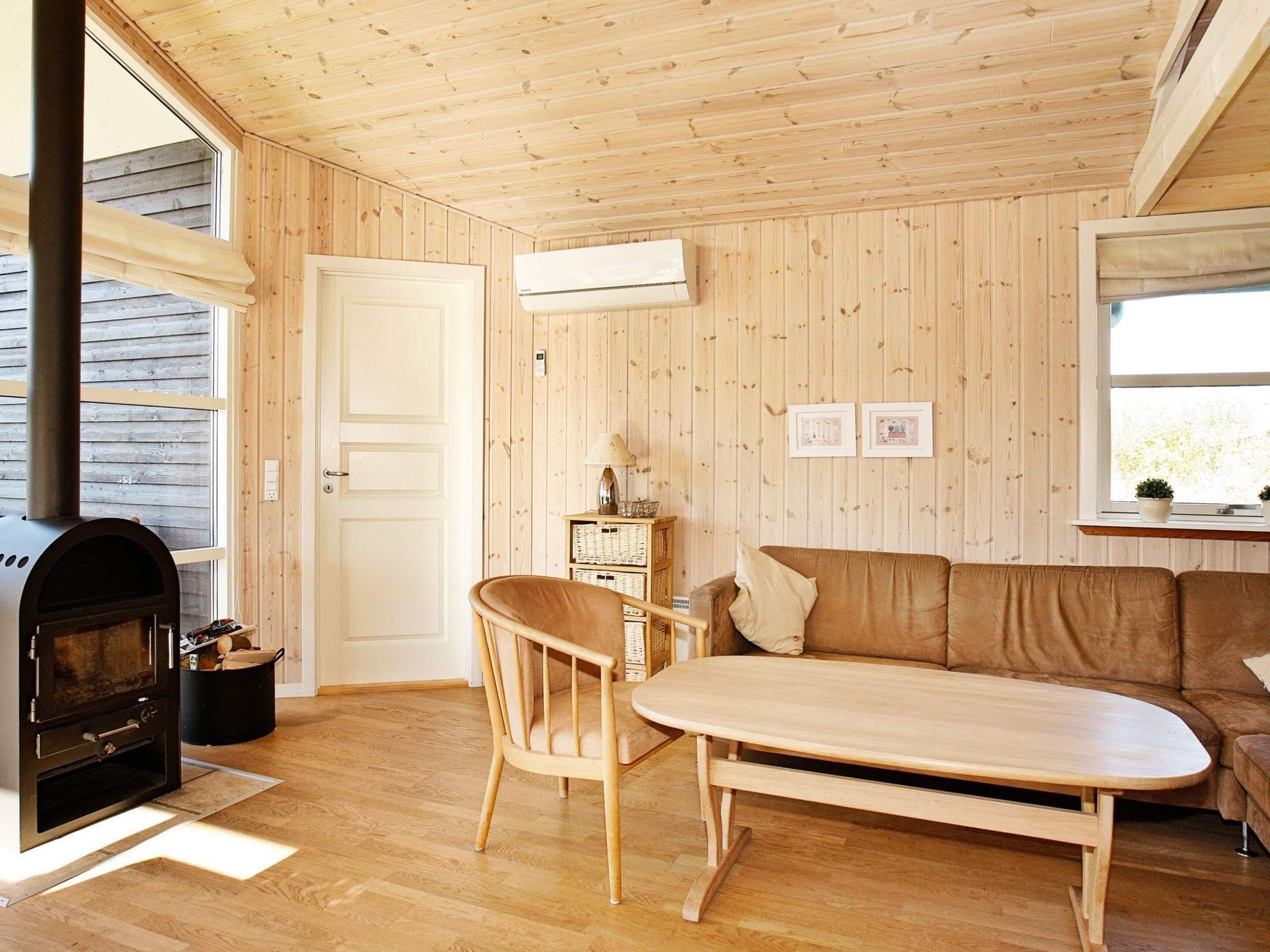 A cozy room with a wooden interior, a sofa, a table, a chair, and a wood-burning stove.