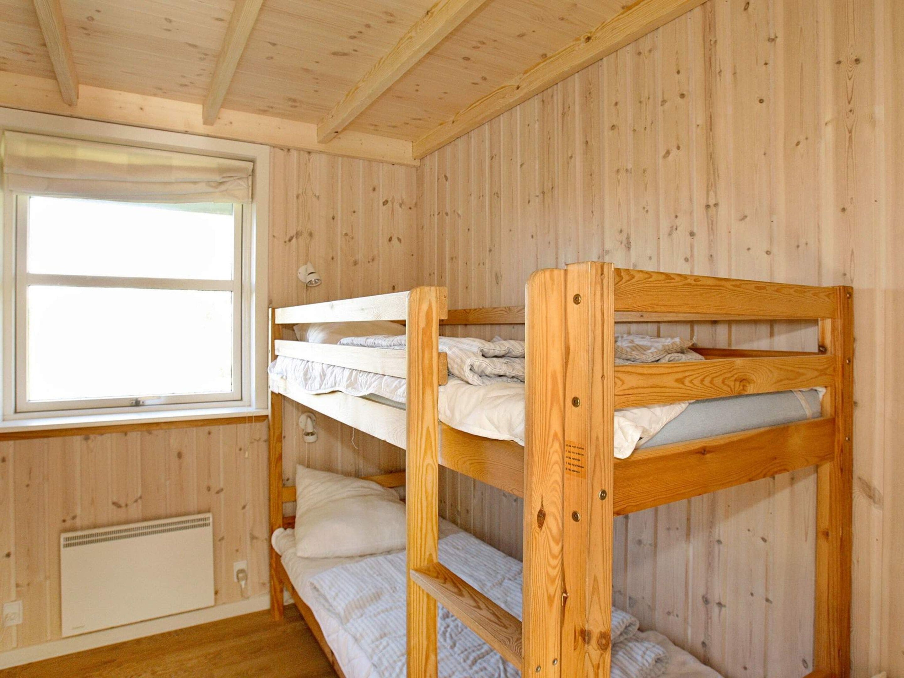Habitación con literas, paredes de madera, una ventana y un radiador.