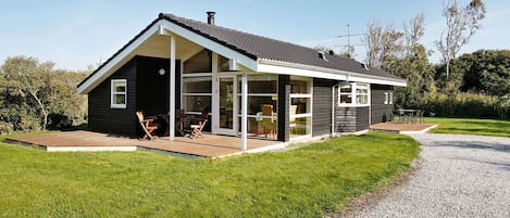 Une maison moderne dotée d’un patio couvert, de grandes fenêtres et d’une allée gravillonnée.