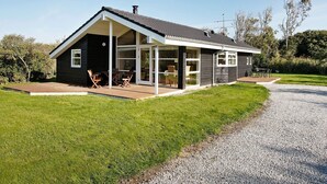 Una casa moderna con patio cubierto, ventanas amplias y camino de entrada de grava.