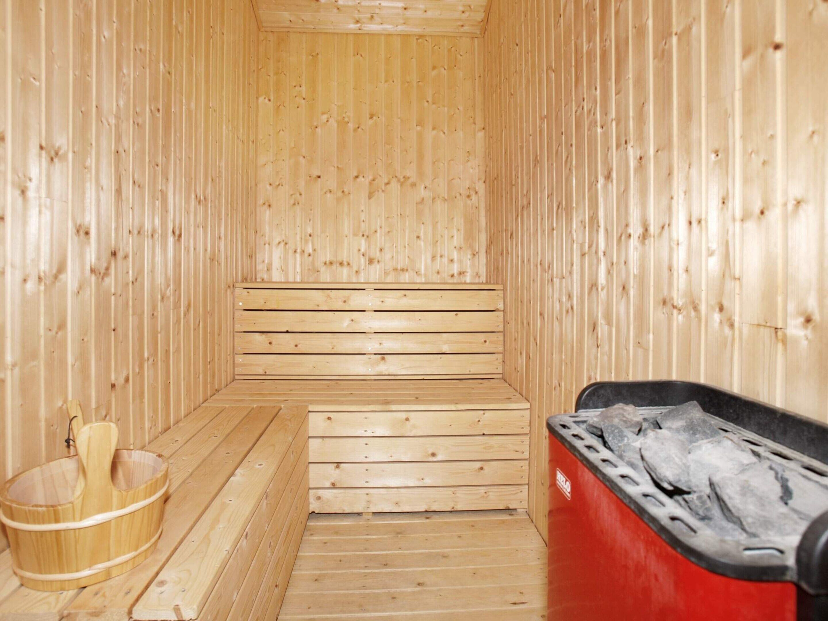 A sauna room with wooden benches and a red sauna heater.