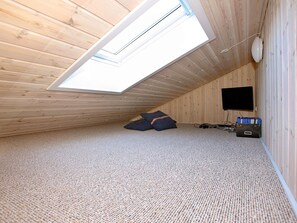 Quarto com teto inclinado, claraboia, televisão e espaço de armazenamento.