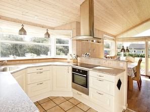A kitchen with wooden cabinets, a built-in oven, and a large window overlooking a garden. - 5 Star Holiday Home in Vestervig (Vestervig)