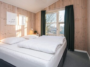 Un dormitorio con una cama grande, una mesita de noche con lámpara y una ventana con cortinas.
