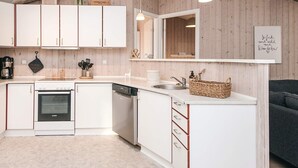 A modern kitchen with white cabinets, a dishwasher, and a built-in oven. There is a wooden wall paneling, a hanging light fixture, and a basket on the countertop. - 8 Person Holiday Home in Borkop (Borkop)