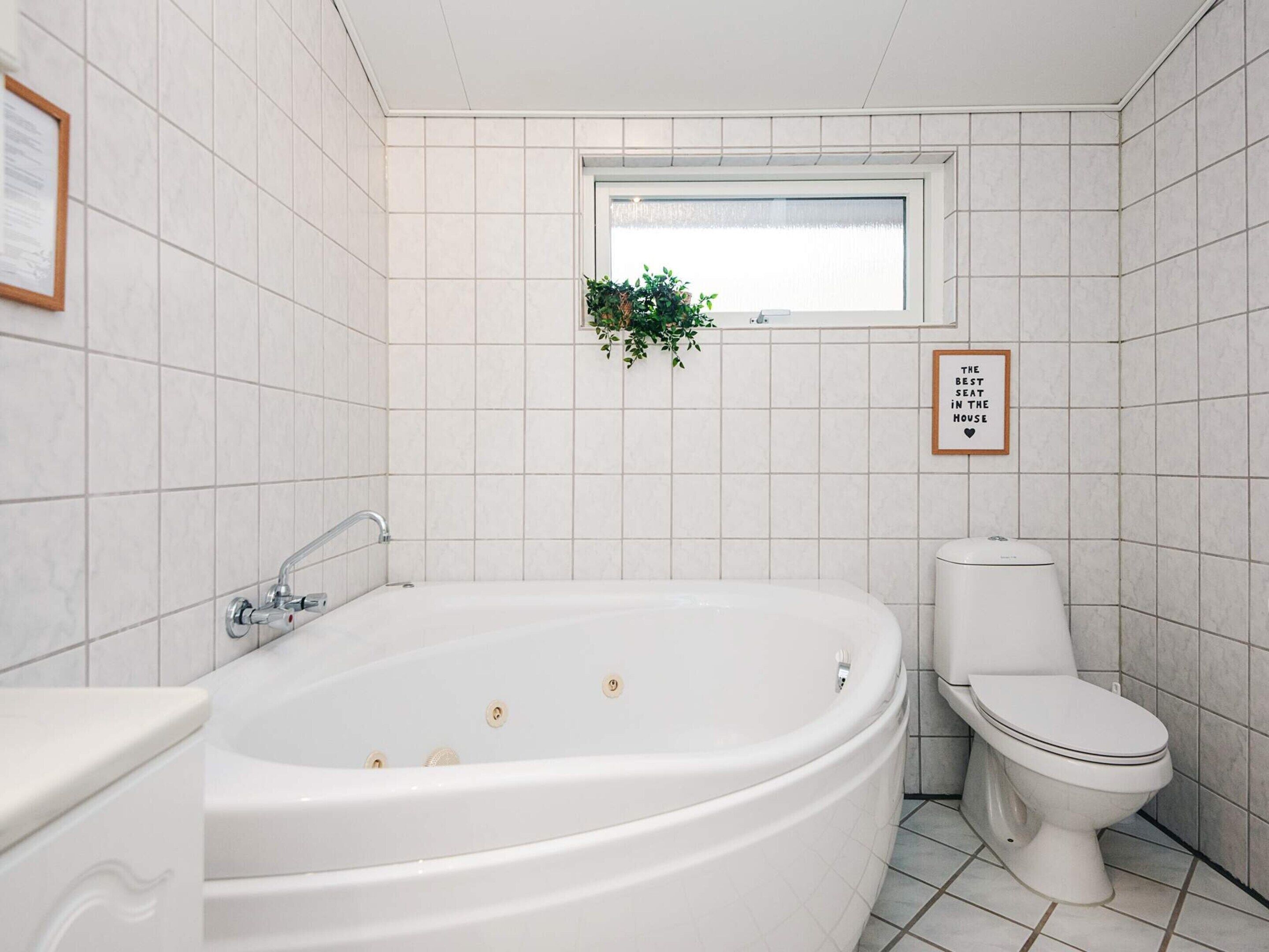 A bathroom with a freestanding bathtub, a toilet, and a window with a plant.