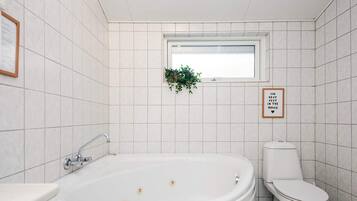 A bathroom with a freestanding bathtub, a toilet, and a window with a plant.
