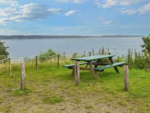 Ein Picknicktisch mit einem Seilzaun in einer grünen Wiese mit Blick auf einen See.