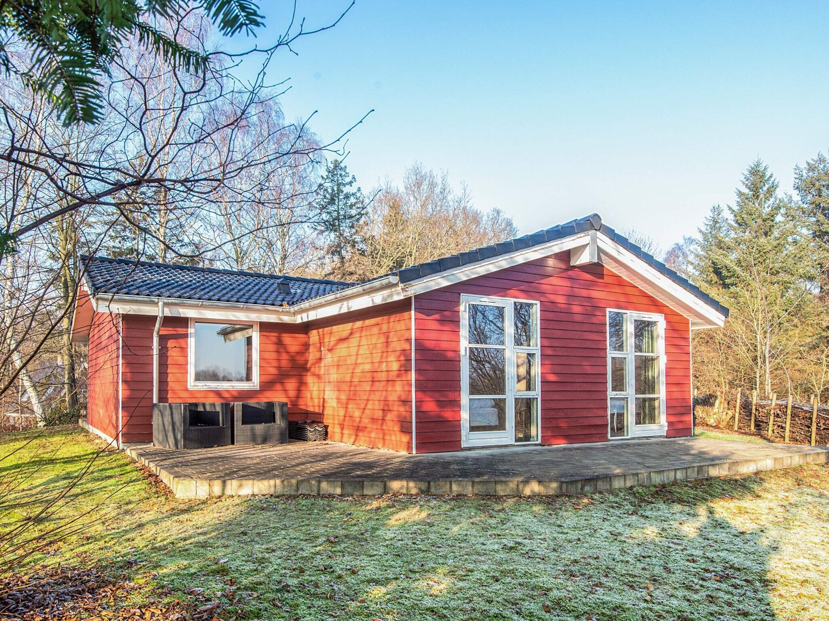 A red wooden house with a porch, large windows, and a sloped roof.