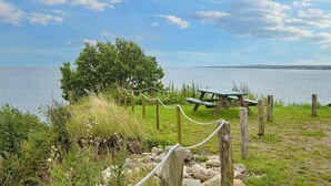 A picnic area with a bench and rope barrier, overlooking a body of water with a distant shoreline. - 8 Person Holiday Home in Borkop (Borkop)