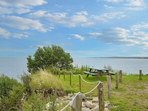 A picnic area with a bench and rope barrier, overlooking a body of water with a distant shoreline.