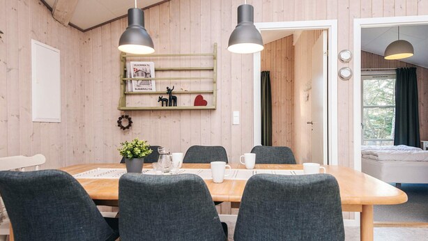 Una habitación revestida de paneles de madera con una mesa de comedor lista para seis comensales, sillas oscuras e iluminación colgante.