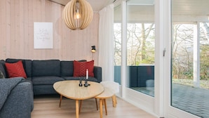 Una sala de estar moderna con un sofá gris, una mesa de centro redonda de madera y una lámpara colgante.
