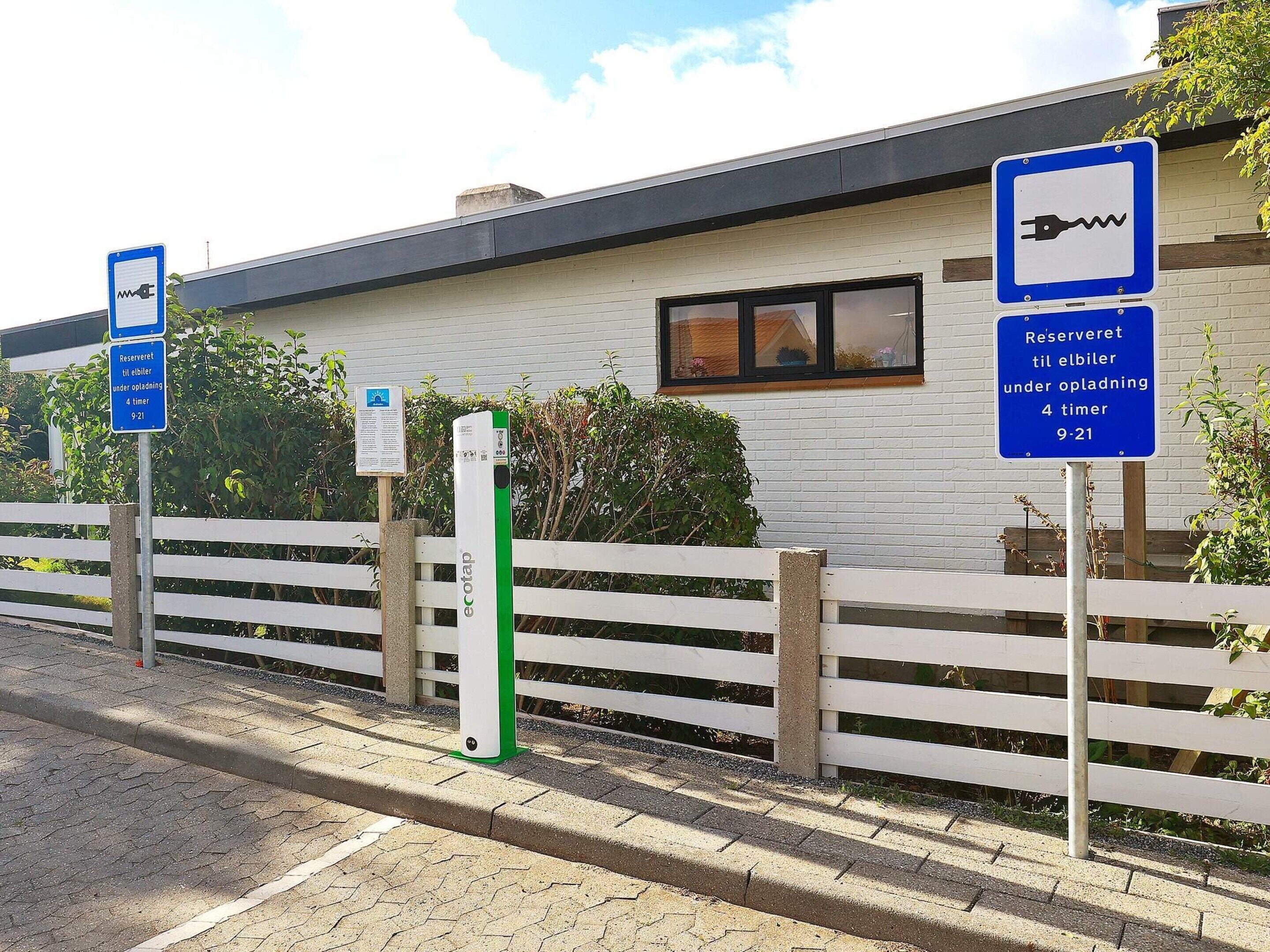 Un espace de stationnement équipé de bornes de recharge pour véhicules électriques et délimité par une clôture blanche.