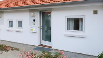 A white building with a red-tiled roof, a glass door, and two windows.