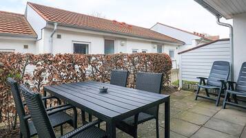 Une terrasse extérieure avec une table et des chaises, une haie et une maison en arrière-plan.