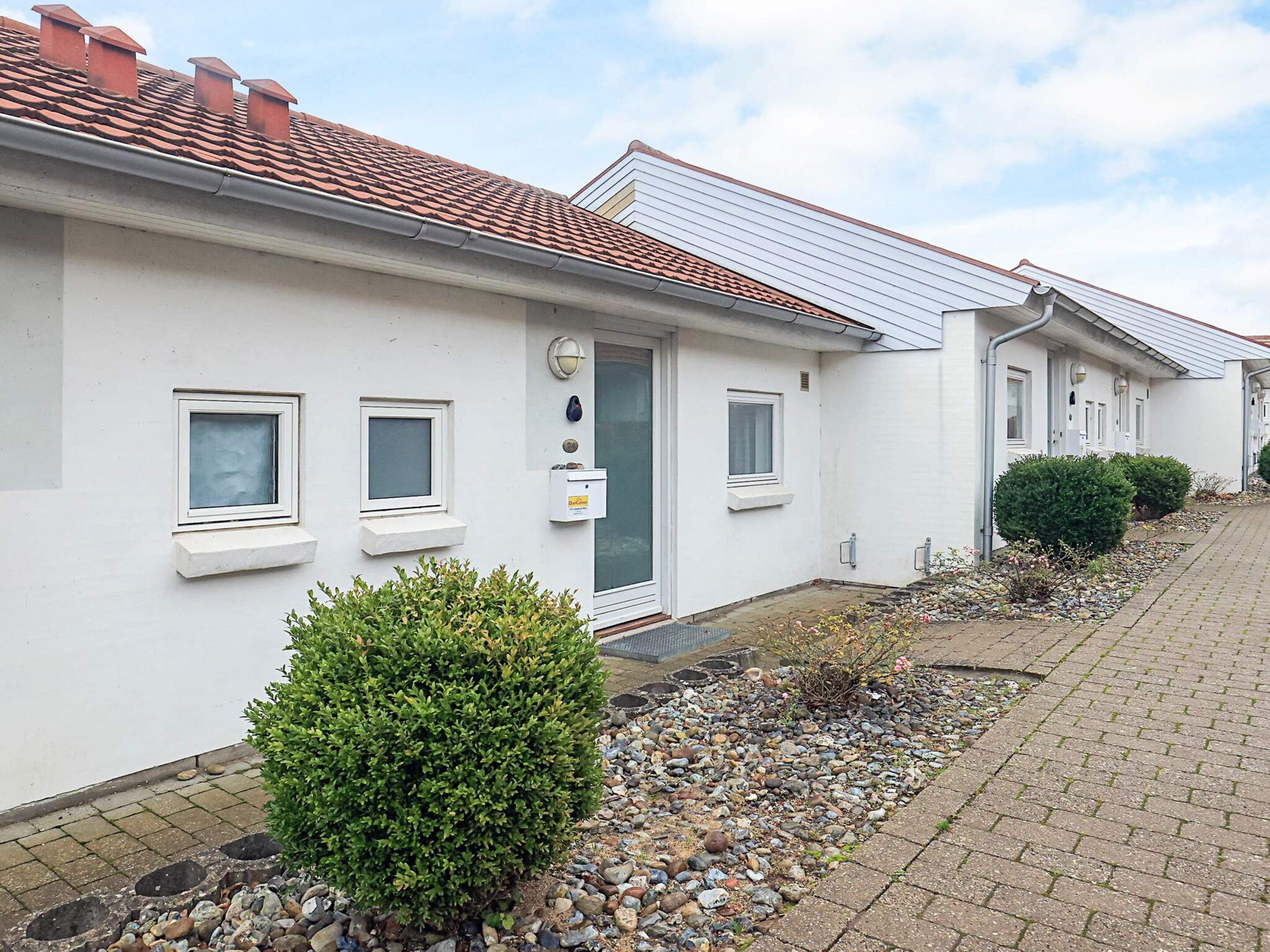 A row of white houses with red-tiled roofs, small windows, and a gravel pathway.