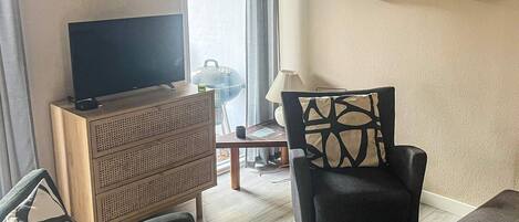 Una sala de estar con una televisión de pantalla plana, un mueble de madera, dos sillas, una mesita y un sofá.