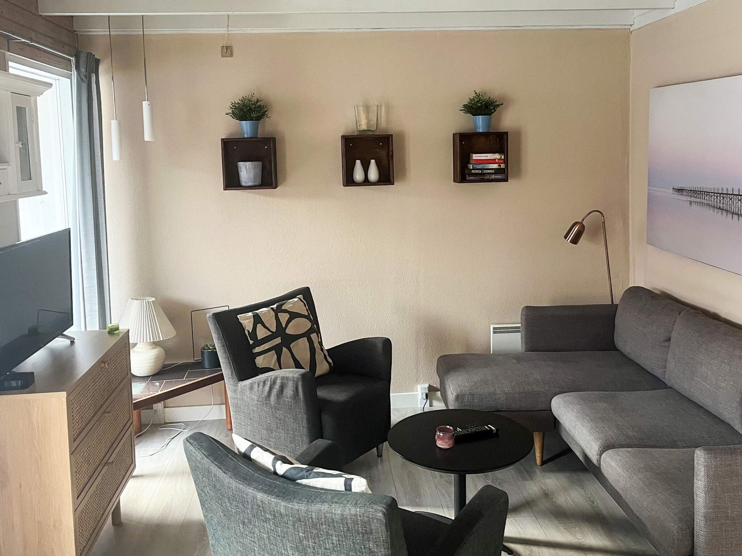 A modern living room with a grey sofa, a black armchair, a small round coffee table, and a television on a wooden cabinet.