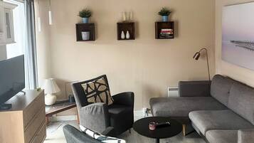 A modern living room with a grey sofa, a black armchair, a small round coffee table, and a television on a wooden cabinet.