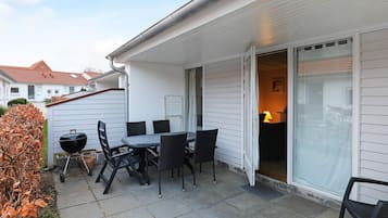 An outdoor patio with a table and chairs, a barbecue grill, and a sliding glass door leading to a room.