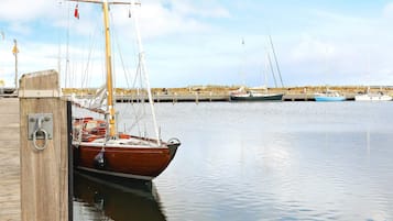 Un muelle de madera con una embarcación amarrada, agua tranquila y una costa distante con otras barcas.
