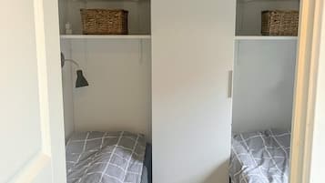 Una habitación con dos camas, cada una con una colcha gris y blanca a cuadros. Hay cestas de mimbre en los estantes superiores a las camas.