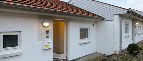A residential building with a tiled roof, a white exterior, and a door leading to a covered entrance.