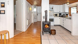 A modern kitchen with a wood-burning stove, white cabinets, and a wooden floor.