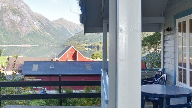 A balcony with a table and chairs, overlooking a red building with a mountain backdrop. - 4 Person Holiday Home in Folkestad (Volda)